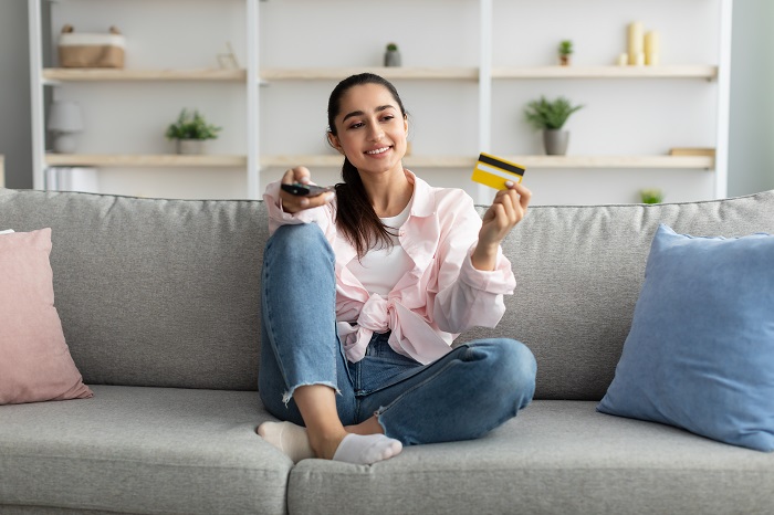 woman holding tv remote in one hand and a debit card in the other
