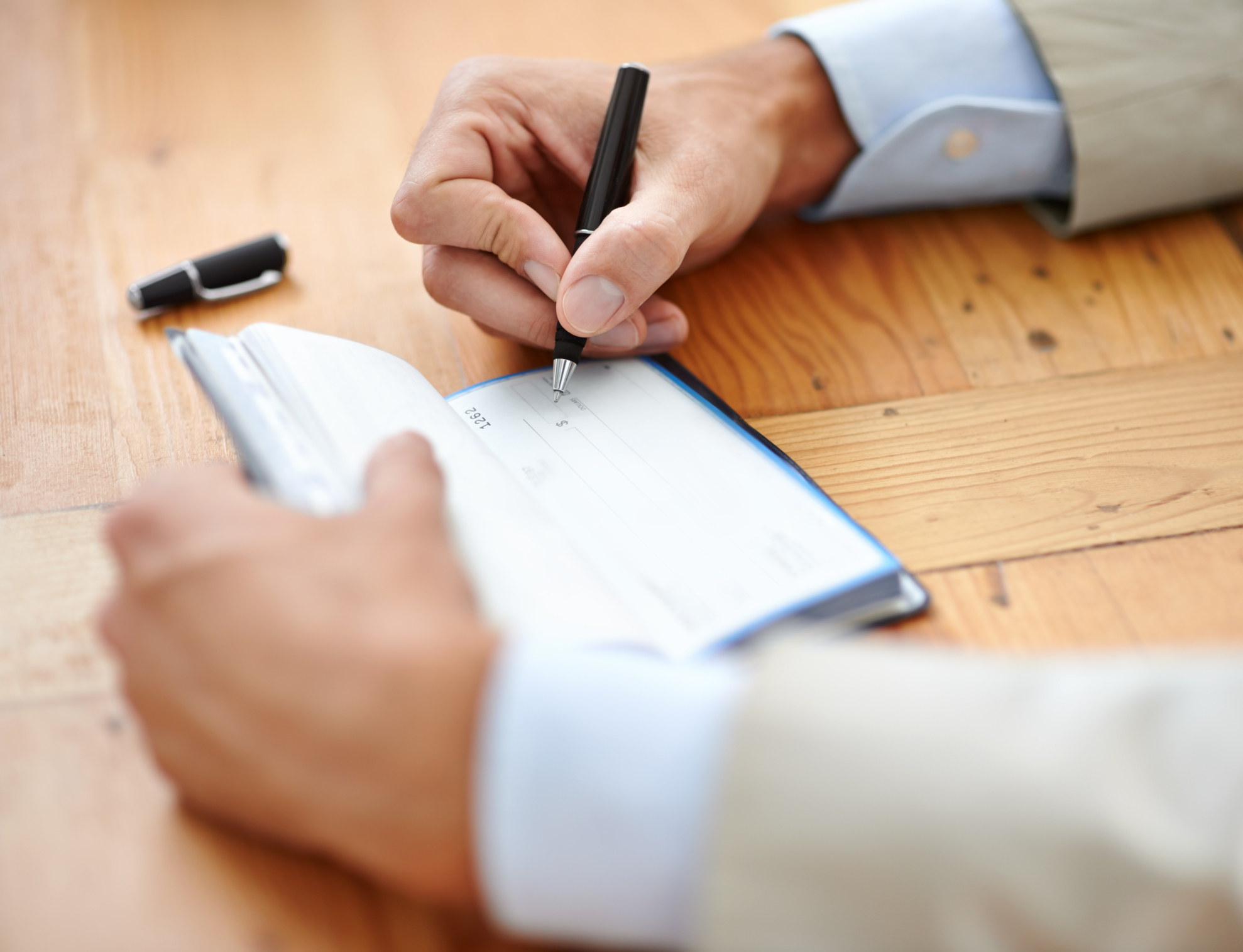 image of someone's forearms and hands at a table writing a check